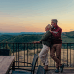 Ein älteres Pärchen steht auf einer Terasse und schaut in die Ferne bei Sonnenuntergang